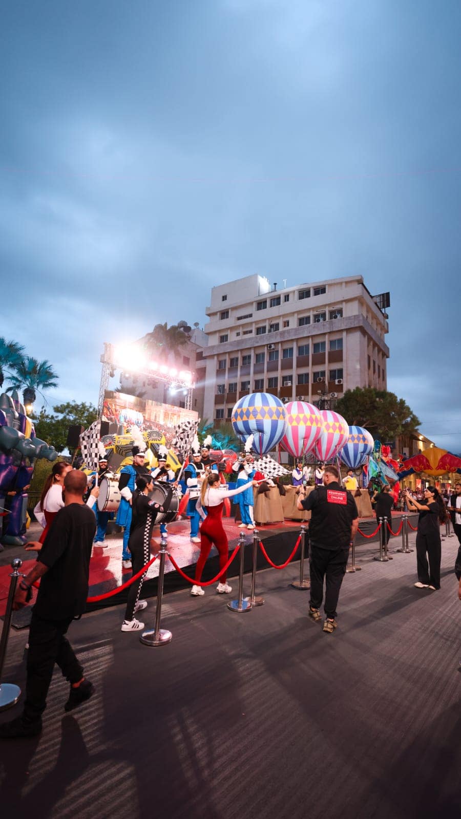 The crowd along the red carpet at dusk, balloons and the stage lights ahead
