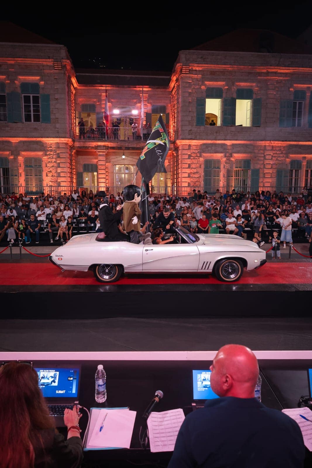 A white convertible on the red stage in front of the lit-up crowd at night
