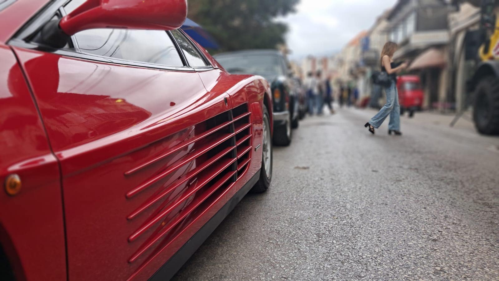 A red Ferrari Testarossa nosing down the souk street between the crowd