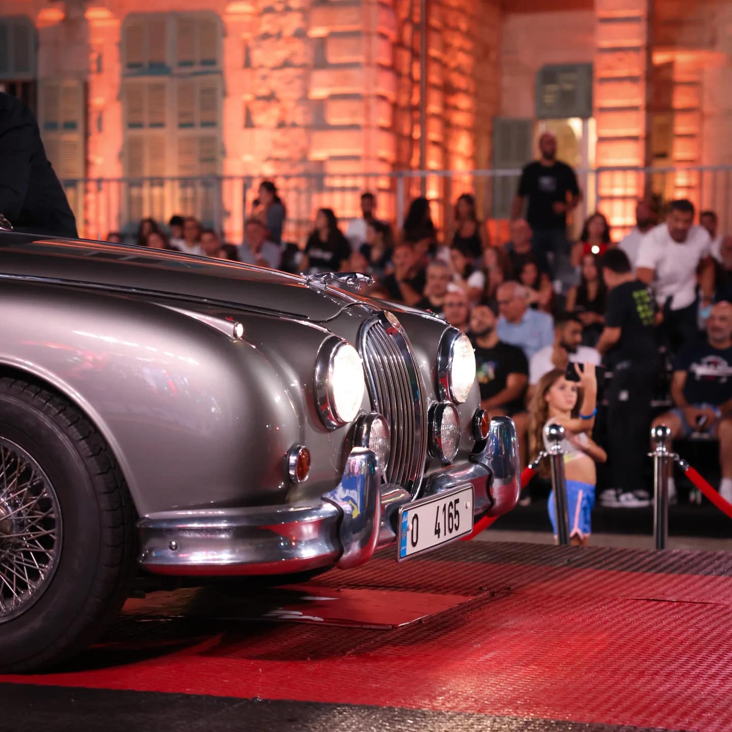A grey Jaguar rolling down the red carpet past the crowd