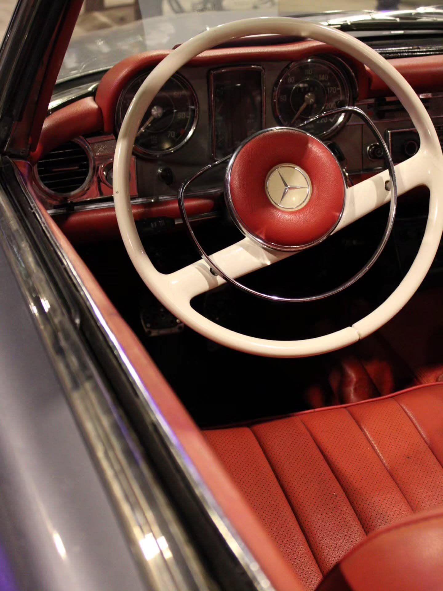 A cream Mercedes steering wheel over red leather